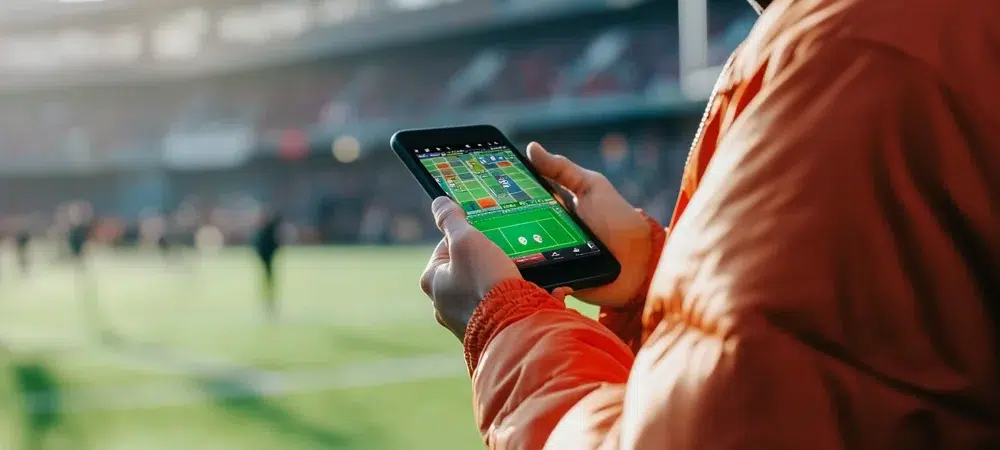Una persona que apuesta al fútbol usando una aplicación móvil mientras está afuera en un día muy cálido